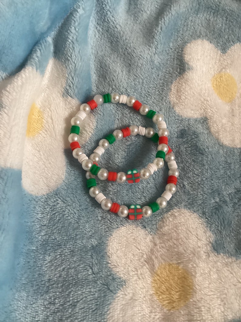 May include: Two beaded bracelets with white, red and green beads. Each bracelet has a small red and green gift box charm.