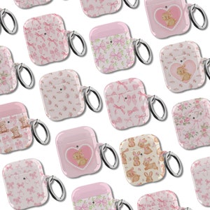 May include: Assortment of pink and white Airpod cases with various designs including bows, flowers, and teddy bears. Each case has a silver ring attached for a keychain.