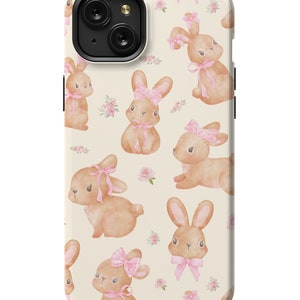 May include: A cream-colored phone case with a repeating pattern of brown bunnies wearing pink bows and pink flowers. The case has a black camera cutout.