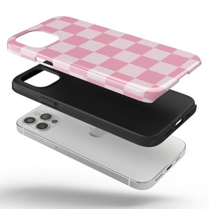 May include: A pink and white checkered phone case for an iPhone 13 Pro Max. The case is shown in three parts: the phone case, the black bumper, and the phone itself.