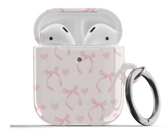 May include: White Airpods case with a pink and white pattern of hearts and bows. The case has a silver ring attached to it.