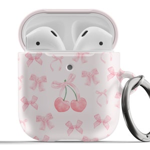 Op de afbeelding: Een roze en witte Airpods-hoes met een kersen- en strikmotief. De hoes heeft een zilveren ring.