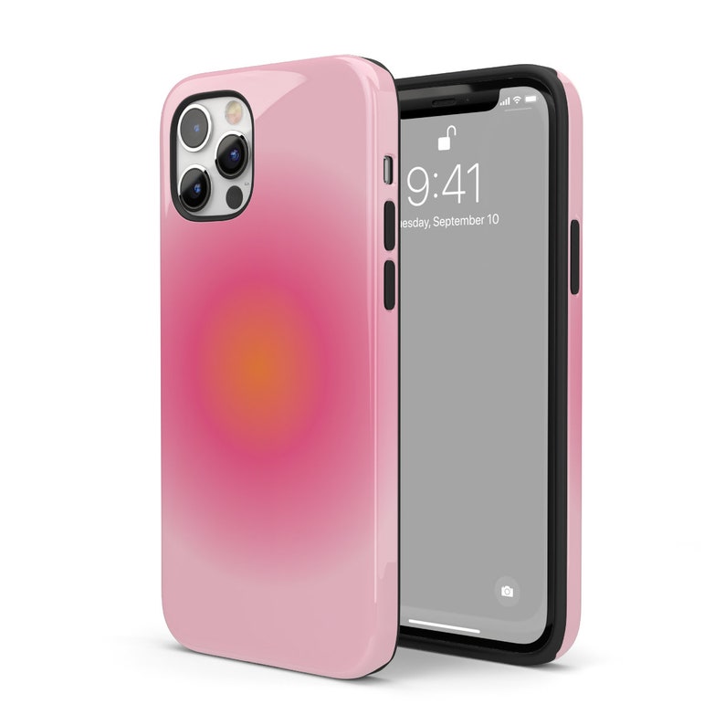 K&ouml;nnte beinhalten: Eine rosa Handyh&uuml;lle mit einem Farbverlauf-Design, das einen gelben und orangen Kreis in der Mitte zeigt. Die H&uuml;lle wird mit einer schwarzen Handyh&uuml;lle gezeigt, deren Bildschirm die Uhrzeit 9:41 und das Datum Dienstag, 10. September anzeigt.