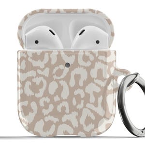 Könnte beinhalten: Ein beige-weißes Airpods-Case mit Leopardenmuster und einem silbernen Metallring.