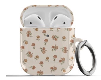 Puede incluir: Una funda blanca para Airpods con un patrón floral con pequeñas rosas marrones sobre un fondo crema. La funda tiene un anillo plateado.
