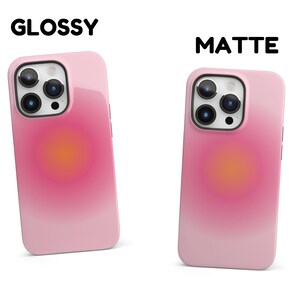 K&ouml;nnte beinhalten: Zwei iPhone-H&uuml;llen, eine gl&auml;nzend und eine matt, beide mit einem Farbverlauf von Pink zu Wei&szlig; und einem kreisf&ouml;rmigen orangen Design. Der Text "GLOSSY" und "MATTE" befindet sich &uuml;ber den H&uuml;llen.