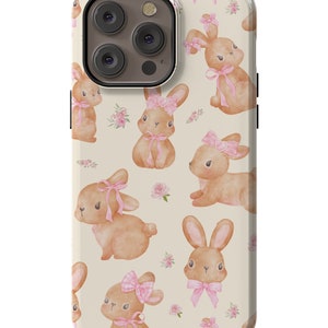 May include: A phone case with a cream background and a pattern of brown bunnies with pink bows. The case has a cutout for the camera lens.