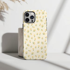 May include: A white iPhone case with a yellow floral pattern. The case has a camera cutout and a black border.