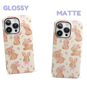 May include: Two iPhone cases with a white background and a pattern of brown bunnies with pink bows. The text "GLOSSY" and "MATTE" are above the cases.