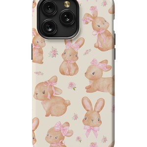 May include: A cream-colored phone case with a repeating pattern of brown bunnies wearing pink bows. The bunnies are surrounded by small pink flowers.