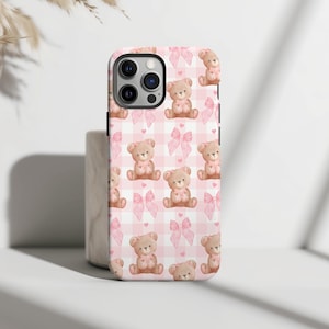 Pode incluir: Capa de telefone xadrez rosa e branca com um padrão de ursos de pelúcia marrons usando laços rosa.