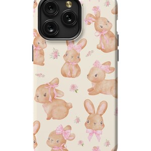 May include: A phone case with a pattern of brown bunnies wearing pink bows on a cream background.