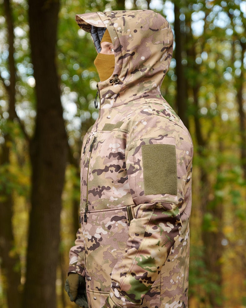 May include: A camouflage jacket with a hood and a green patch on the sleeve. The jacket is made of a soft, water-resistant material and is perfect for outdoor activities.