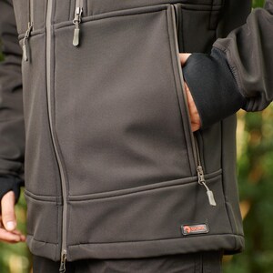 May include: A dark gray softshell jacket with a zipper closure and multiple pockets. The jacket has a logo on the bottom right pocket that says "SOKIL".