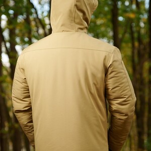 May include: A tan hooded jacket with a zipper closure. The jacket has a smooth, textured fabric and a zippered pocket on the left sleeve.