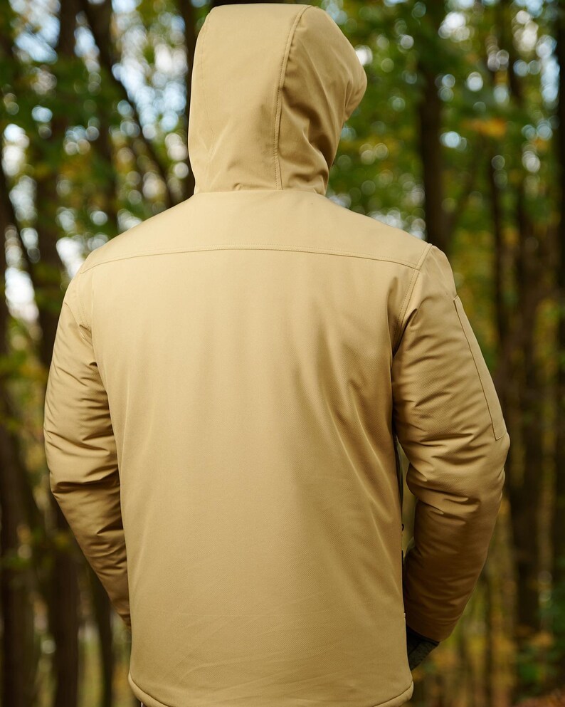 May include: A tan hooded jacket with a zipper closure. The jacket has a smooth, textured fabric and a zippered pocket on the left sleeve.