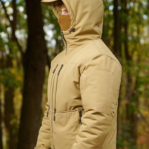 May include: A tan hooded jacket with a zipper closure and multiple pockets. The jacket has a high collar and a drawstring hood.