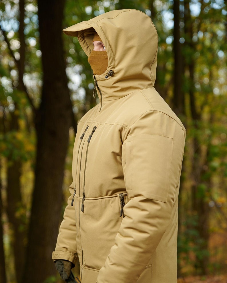 May include: A tan hooded jacket with a zipper closure and multiple pockets. The jacket has a high collar and a drawstring hood.
