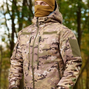 May include: A camouflage jacket with a brown hooded sweatshirt underneath. The jacket has a zipper closure and multiple pockets.
