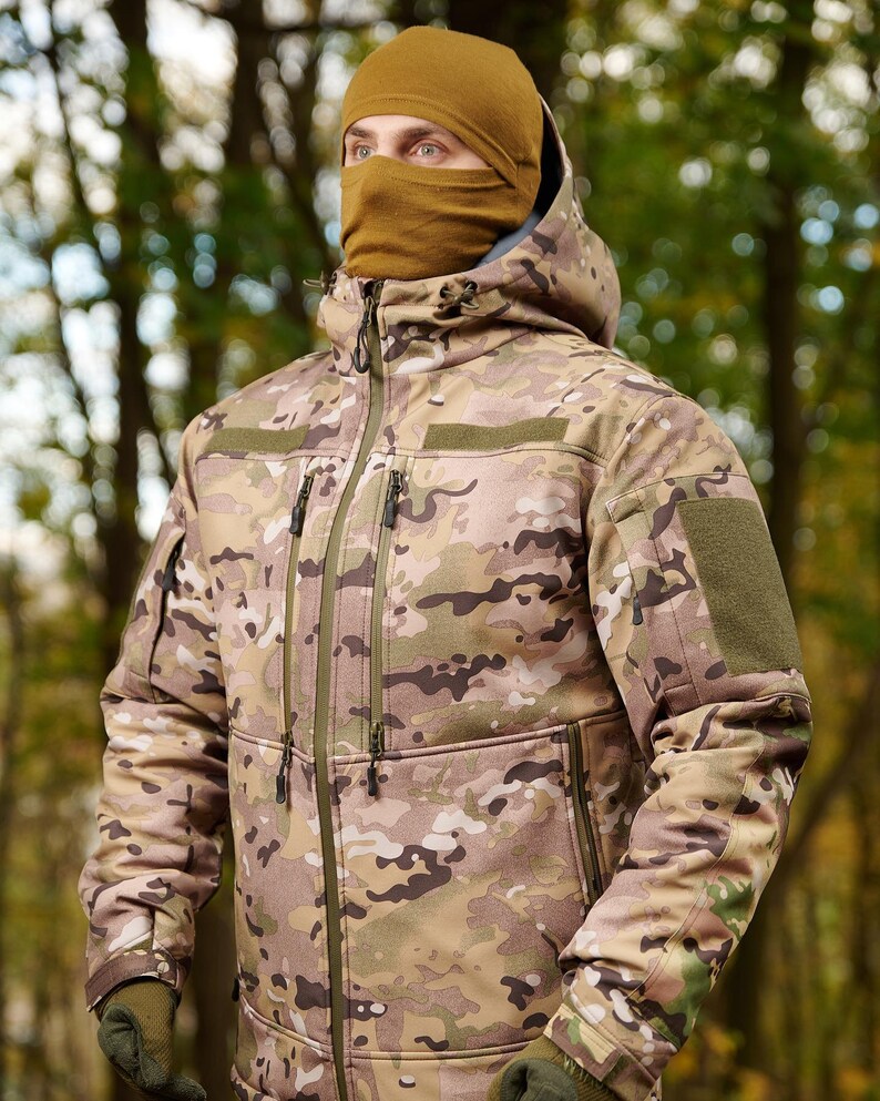 May include: A camouflage jacket with a brown hooded sweatshirt underneath. The jacket has a zipper closure and multiple pockets.