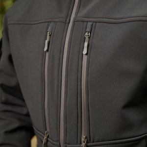 May include: A black softshell jacket with multiple zippered pockets and a contrasting gray zipper trim.