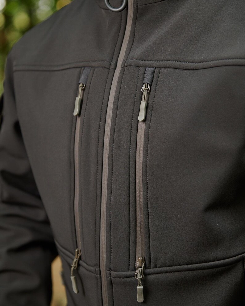 May include: A black softshell jacket with multiple zippered pockets and a contrasting gray zipper trim.