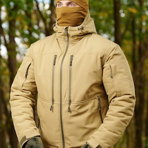 May include: A tan jacket with a zipper closure and multiple pockets. The jacket has a hood and is worn over a brown balaclava.