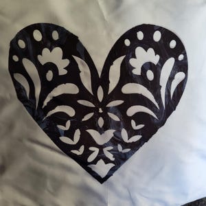 May include: A white cushion with a black and white heart-shaped design. The heart features a floral pattern with intricate details.
