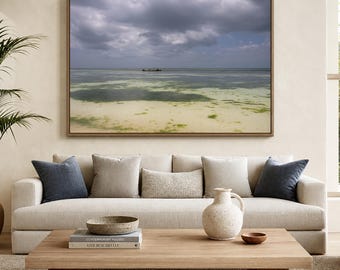 May include: A framed landscape wall art print depicting a calm ocean scene with a small boat on the horizon under a cloudy sky, displayed above a beige sofa with blue and neutral pillows, a wooden coffee table, and a ceramic vase.