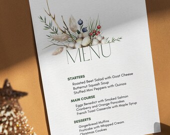 May include: A white menu card with a watercolor illustration of a floral arrangement with cotton, berries, and leaves. The menu card lists the starters, main course, and desserts for a holiday meal. The text on the menu card reads: "STARTERS Roasted Beet Salad with Goat Cheese Butternut Squash Soup Stuffed Mini Peppers with Quinoa MAIN COURSE Eggs Benedict with Smoked Salmon Cranberry and Orange Pancakes French Toast Casserole with Maple Syrup DESSERTS Gingerbread Muffins Fruitcake with Whipped Cream Christmas Cookies"
