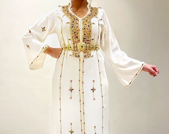 May include: A white long-sleeved dress with gold embroidery and a gold belt. The dress has a V-neckline and a long, flowing skirt.