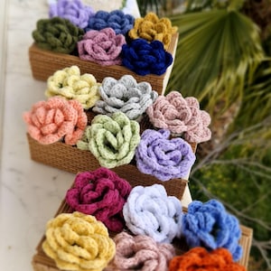 Puede incluir: Una colección de posavasos de ganchillo con forma de flor en varios colores, incluyendo rosa, azul, verde, amarillo y naranja. Los posavasos están dispuestos en tres filas sobre una cesta tejida.