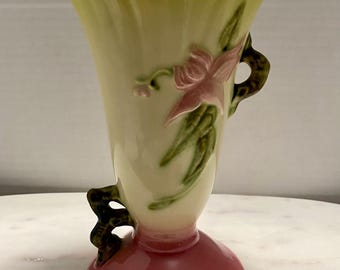 May include: A vintage ceramic vase with a green and yellow body, pink floral design, and green handles. The vase has a pink base.