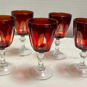 May include: Set of five red glass wine glasses with a clear stem and base. The glasses have a textured, faceted design.