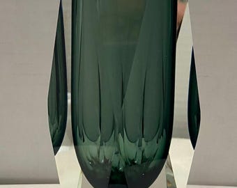Könnte beinhalten: Eine dunkelgrüne Glasvase mit facettiertem Design. Die Vase hat einen klaren Glasfuß mit geometrischer Form.