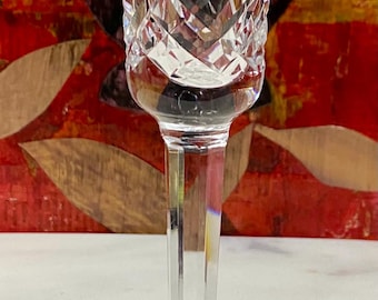 May include: A clear crystal candlestick holder with a starburst design on the base. The stem is long and slender, and the top has a flared opening. The glass is cut with a diamond pattern.