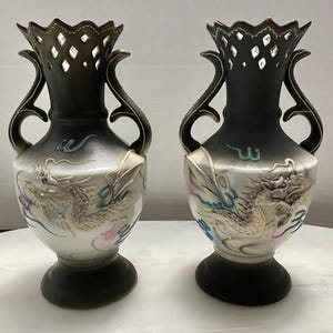 May include: Two black and white ceramic vases with gold dragon designs. The vases have openwork tops and two handles.