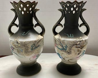Könnte beinhalten: Zwei schwarze und weiße Keramikvasen mit goldenen Drachenmotiven. Die Vasen haben durchbrochene Oberteile und zwei Henkel.
