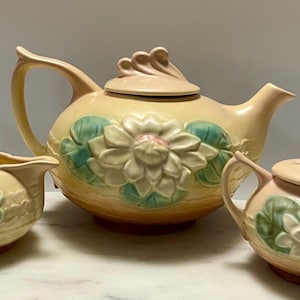 May include: A white ceramic mug with a black handle and the text "But First, Coffee" in a black, handwritten-style font. The mug is on a white surface.