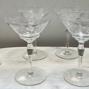 May include: Set of six clear glass martini glasses with etched floral designs. The glasses have a stemmed base and a wide, shallow bowl.