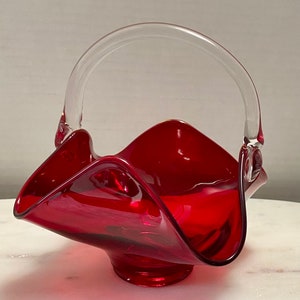 May include: A red glass bowl with a clear glass handle. The bowl has a wavy, organic shape and is perfect for serving fruit or snacks.