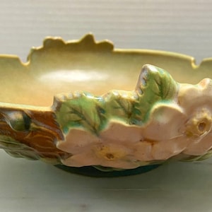 May include: A vintage ceramic bowl with a green, brown, and pink floral design. The bowl is shaped like a leaf and has a raised rim. The flowers are in bloom and have a delicate, feminine look.
