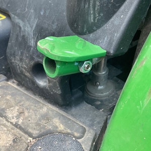 May include: A green plastic attachment with a metal bolt and a round opening. The attachment is mounted on a black surface.