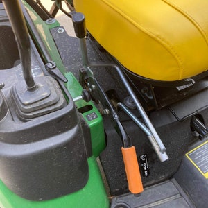 May include: Close-up of a green and black tractor with a yellow seat. The tractor has a black lever with an orange handle and a silver lever with a black handle. The levers are labeled "FWD" and "REV".