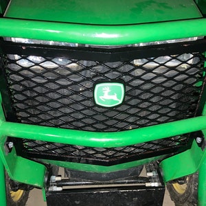 May include: Green tractor with a black metal grille and a green John Deere logo. The grille is made of a diamond-shaped wire mesh.