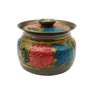 Op de afbeelding: Een decoratieve pot met deksel en bloemmotief. De pot heeft een donkere metalen basis en deksel, versierd met rode, blauwe en roze bloemen. De bloemen zijn geplaatst tegen een gouden achtergrond.