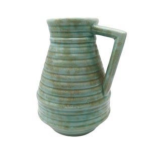 May include: A turquoise ceramic pitcher with a ribbed design. The pitcher has a handle and a wide opening. The color is a muted turquoise with brown accents. The pitcher is likely used for serving beverages or as a decorative item.