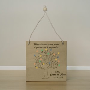 Peut inclure: Une pancarte en bois avec un arbre et des points colorés, un message qui dit "Merci de nous avoir aidés à grandir et à apprendre", et le texte "CM2 Classe de Valerie 2023-2024".
