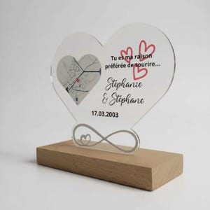 Può includere: Targa a forma di cuore in acrilico trasparente con mappa e testo "Tu es ma raison préférée de sourire... Stephanie & Stephane 17.03.2003". La targa è su una base di legno con un simbolo dell'infinito.