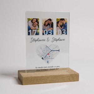 Può includere: Un espositore fotografico personalizzato con tre immagini, date e nomi. Il pannello in acrilico trasparente poggia su una base in legno. Il testo include i nomi "Stéphanie & Stéphane" e la frase "Rendi il mio mondo un po' più luminoso ogni giorno."